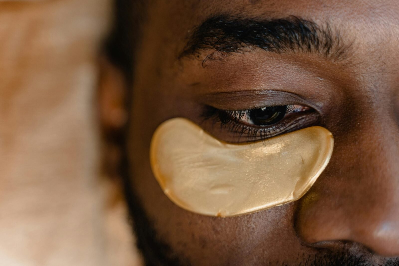 Close-up of a man's eye with a gold under eye patch, focusing on skincare and rejuvenation.