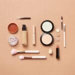 Stylish flatlay of various makeup products on a soft peach background.