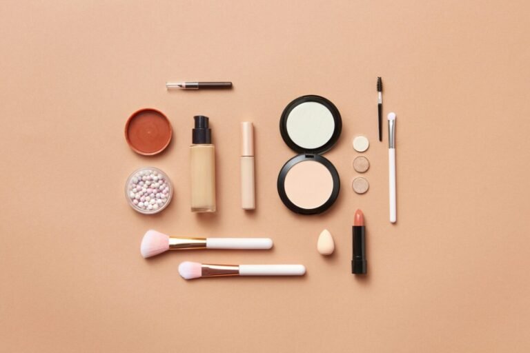 Stylish flatlay of various makeup products on a soft peach background.