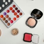 Top view of assorted makeup products including palettes, brushes, and powders on a white surface.